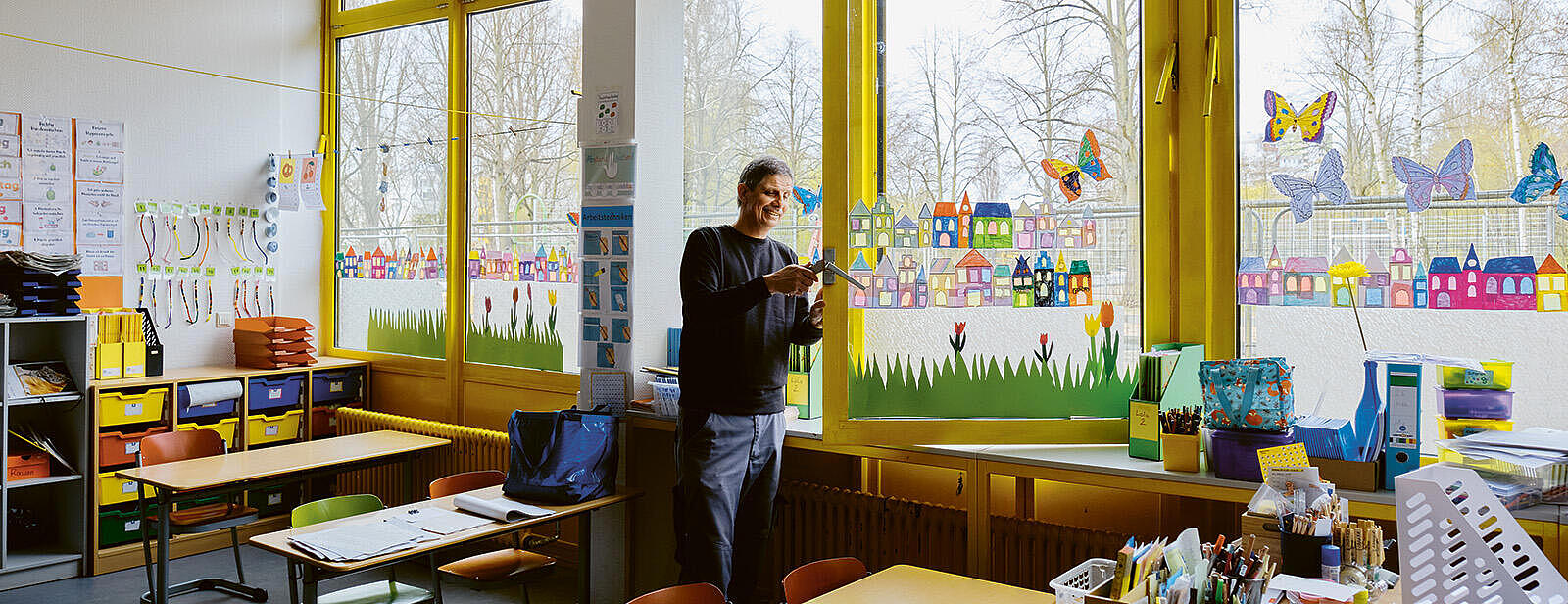 Innenaufnahme: Mann repariert Fenstergriff in Klassenzimmer