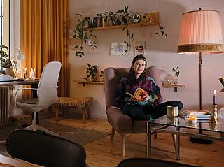 Ein Foto eines renovierten Wohnzimmers in Gesundbrunnen. Mittig sitzt eine Frau mit Buch auf einem Sessel. Links ist ein Schreibtisch vor einem großen Fenster mit Balkon.