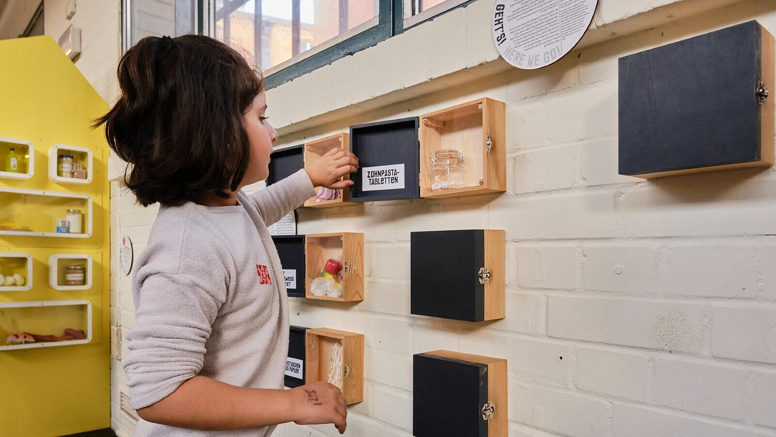 Innenaufnahme: Mädchen öffnet Holzboxen an einer Wand