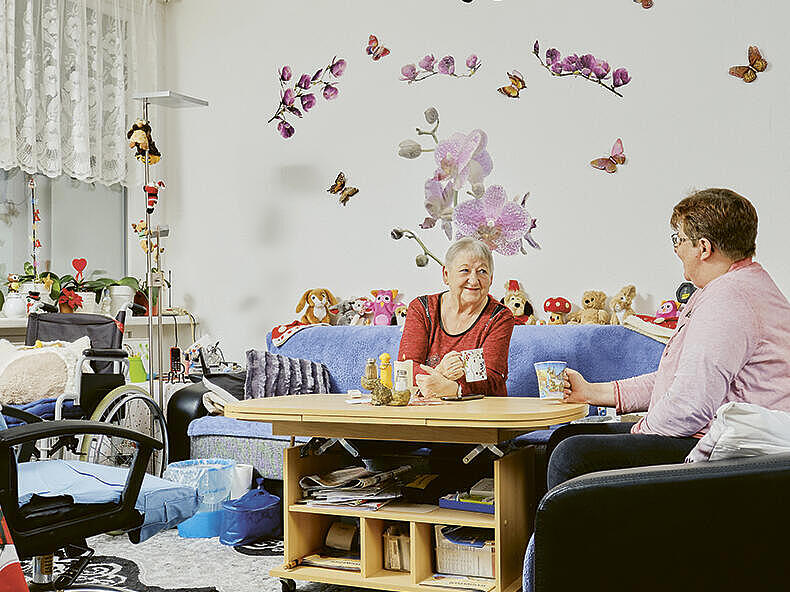 Innenaufnahme: Ältere Frau sitzt in einem weihnachtlich dekorierten Wohnzimmer auf der Couch, ihr gegenüber eine etwas jüngere Frau