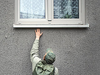 Mann greift unter eine Fensterbank auf der Suche nach einer Spinne