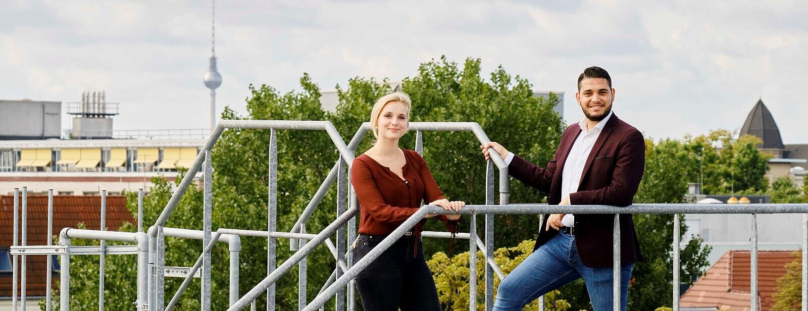 Außenaufnahme: Junge Frau und junge Mann auf Flachdach, im Hintergrund Berliner Fernsehturm