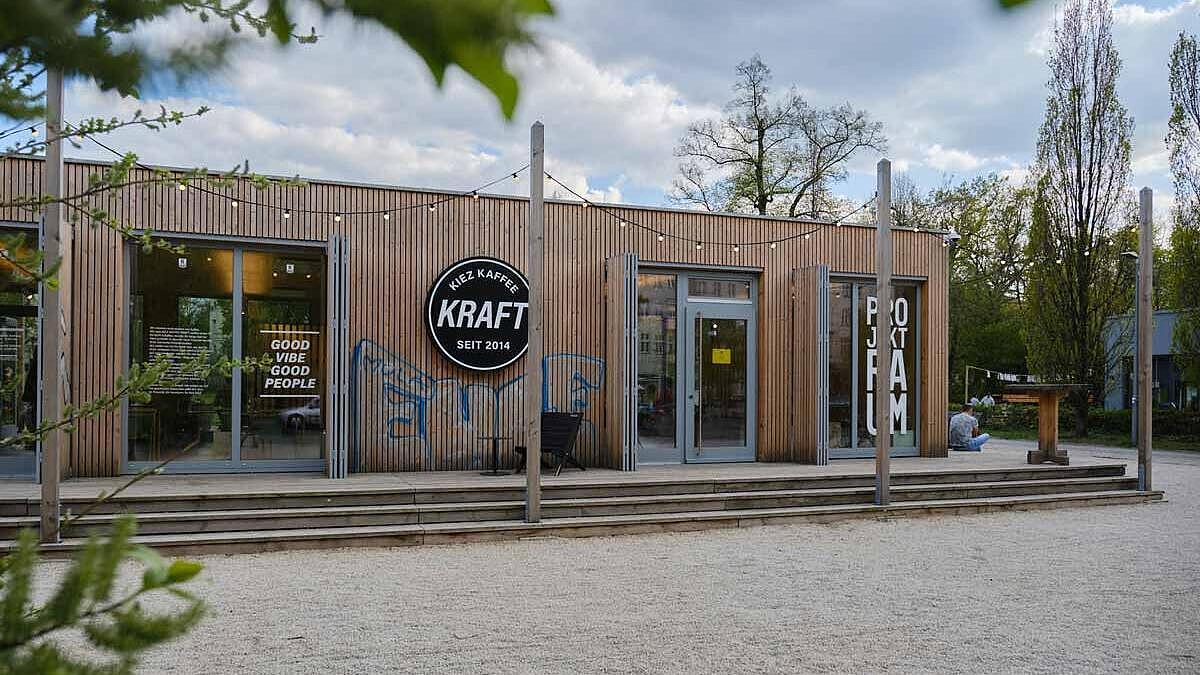 Außenaufnahme: Holzbungalow mit Lichterketten, an der Fassade der Schriftzug Kiez Kaffee Kraft