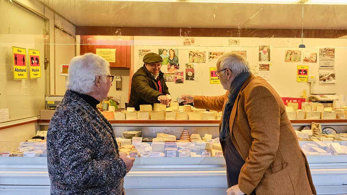 Außenaufnahme: Zwei ältere Männer an einem Käsestand, Verkäufer reicht etwas über die Theke