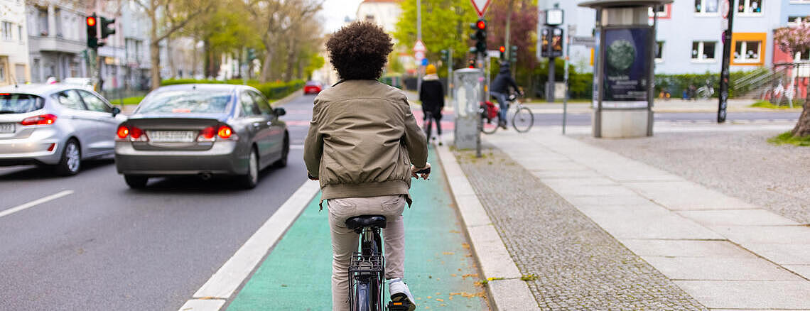 Außenaufnahme: Fahrradfahrender auf Radweg, links Straße mit Autos, rechts Gehweg