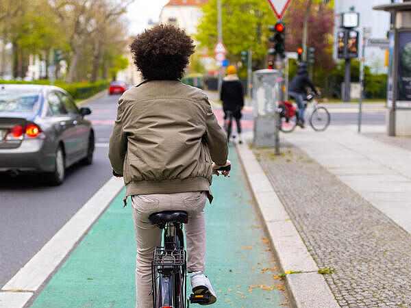 Außenaufnahme: Fahrradfahrender auf Radweg, links Straße mit Autos, rechts Gehweg