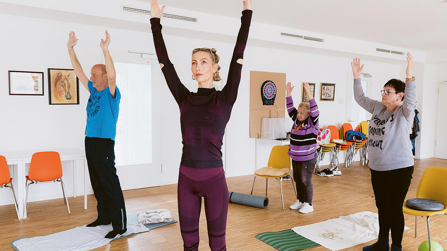 Innenaufnahme: Vier Personen heben die Hände, vor ihnen Yogamatten