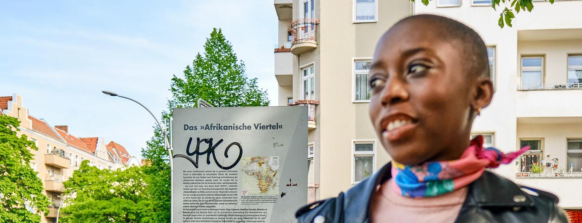 Außenaufnahme: Justice Mvemba vom Verein „Dekoloniale Stadtführungen“, im Hintergrund Infostele zum Afrikanischen Viertel