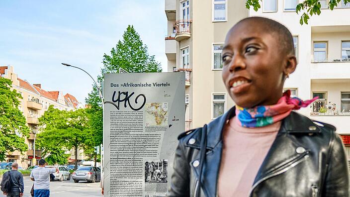 Außenaufnahme: Justice Mvemba vom Verein „Dekoloniale Stadtführungen“, im Hintergrund Infostele zum Afrikanischen Viertel