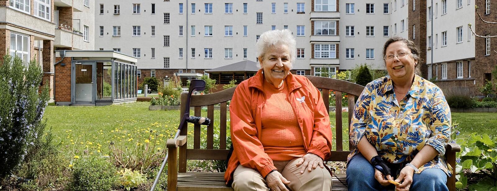 Außenaufnahme: Zwei ältere Frauen auf Gartenbank in grünem Innenhof