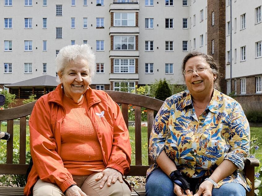 Außenaufnahme: Zwei ältere Frauen auf Gartenbank in grünem Innenhof