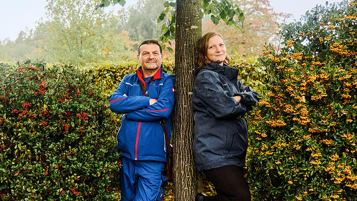 Außenaufnahme: Mann und Frau lehnen sich an Baum, daneben Hecken