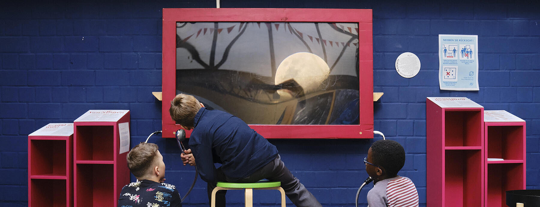 Innenaufnahme: Drei Jungen von hinten vor einer blauen Steinwand