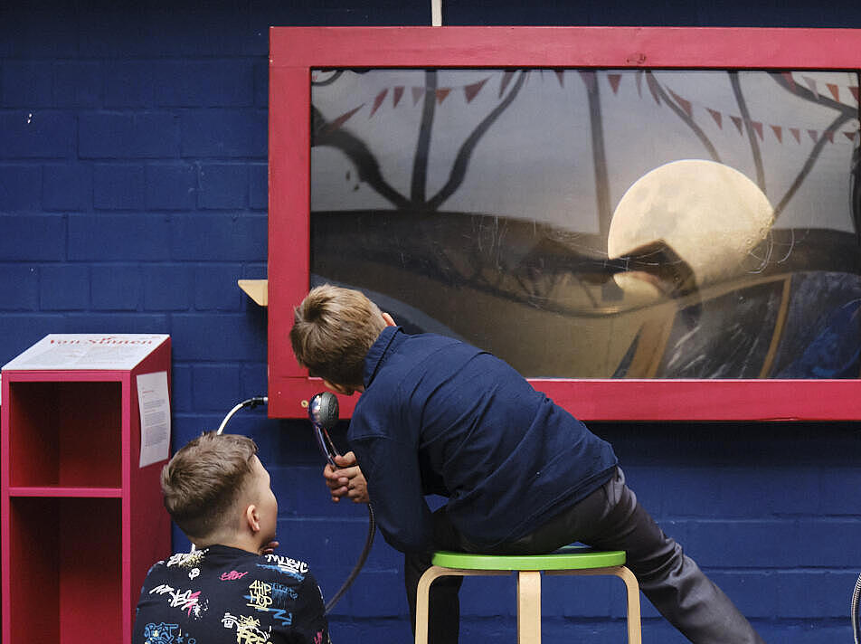 Innenaufnahme: Drei Jungen von hinten vor einer blauen Steinwand