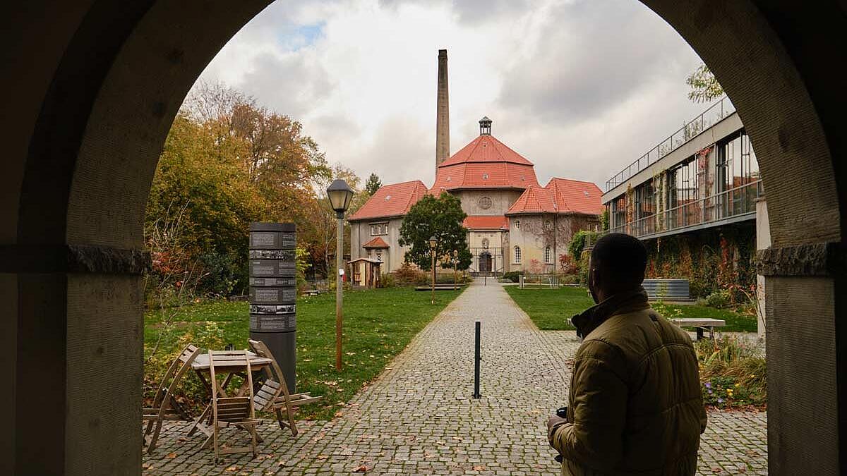 Innenaufnahme: Mann steht im Torbogen, im Hintergrund ein Gebäude mit Schlot