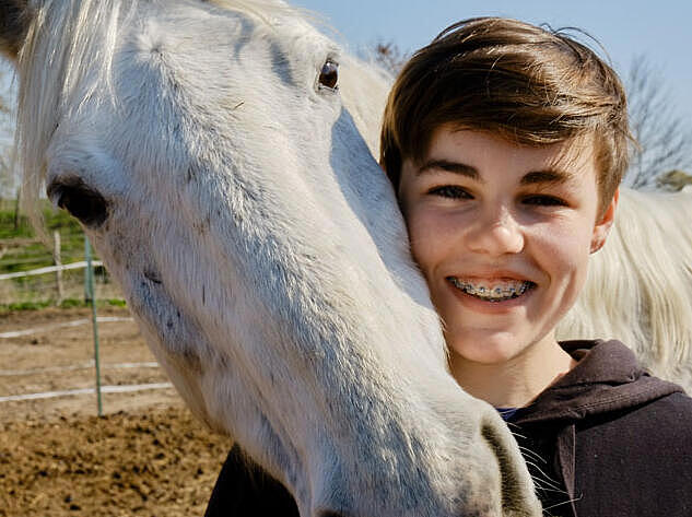 Außenaufnahme: Weißes Pferd legt Kopf auf die Schulter eines Jungen