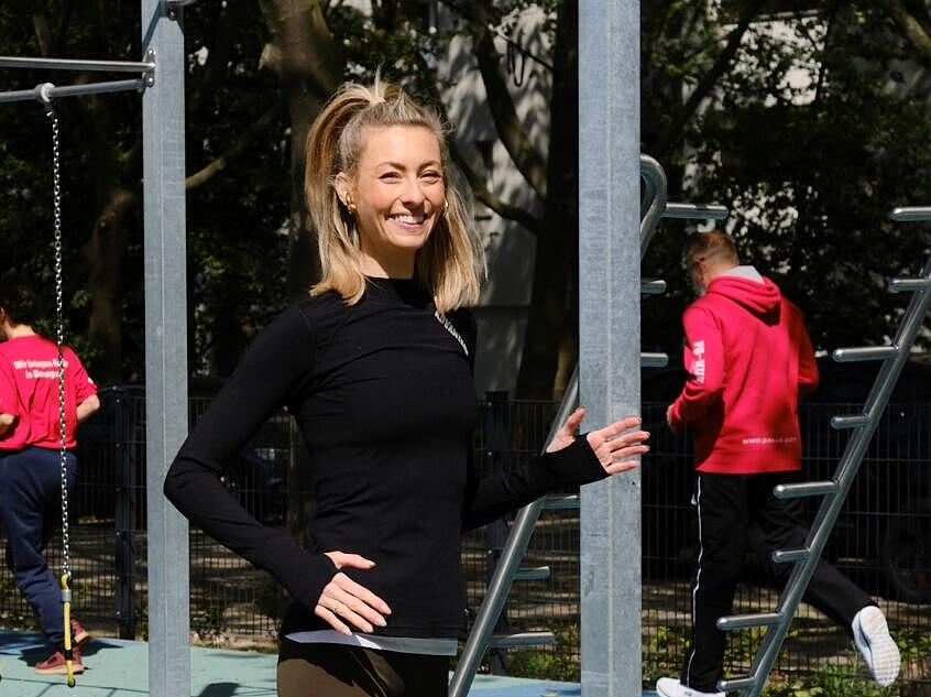 Außenaufnahme: Junge Frau läuft vor Trainingspark mit Sportgeräten